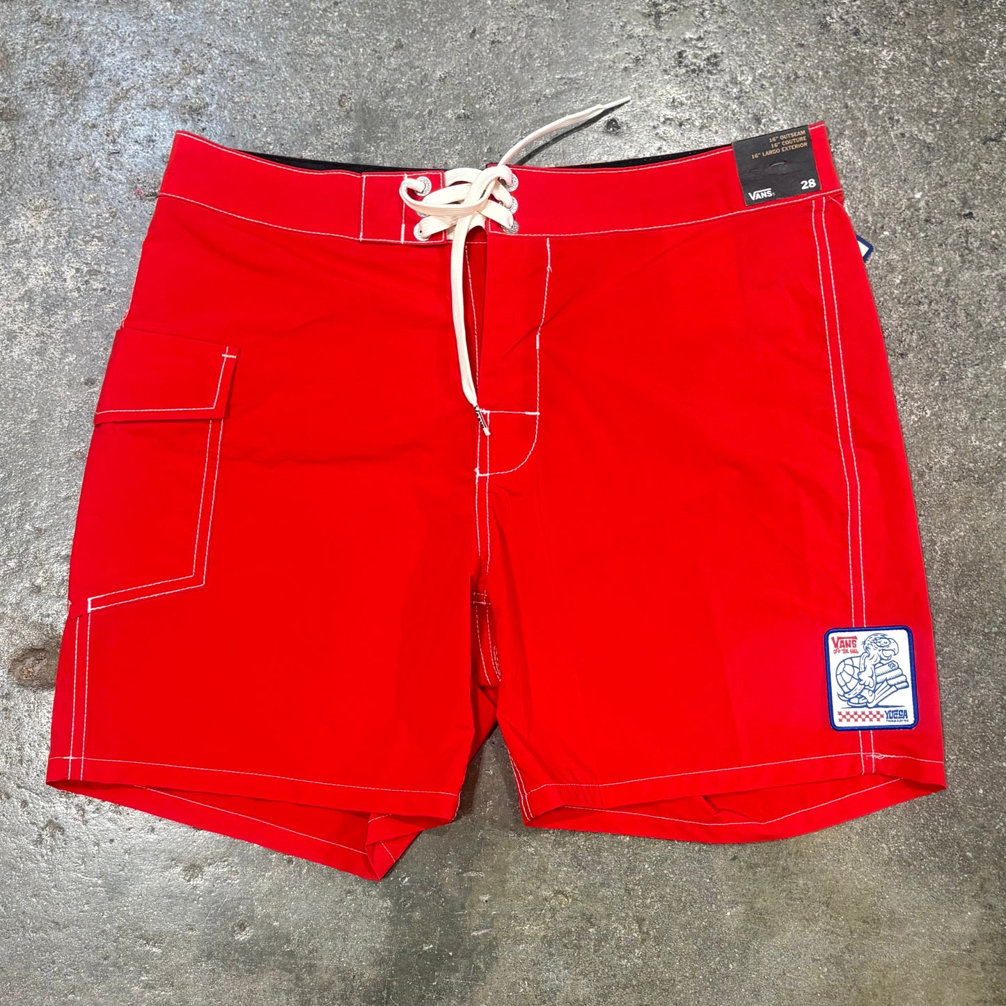 Red board shorts with a patch on a concrete surface