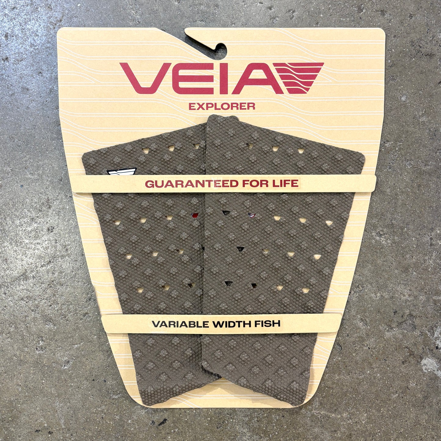 A VEIA Explorer variable width fish tail pad in dark gray with a diamond pattern, mounted on its original beige cardboard backing against a gray concrete floor.