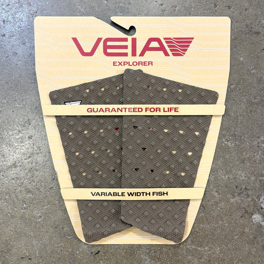 A VEIA Explorer variable width fish tail pad in dark gray with a diamond pattern, mounted on its original beige cardboard backing against a gray concrete floor.