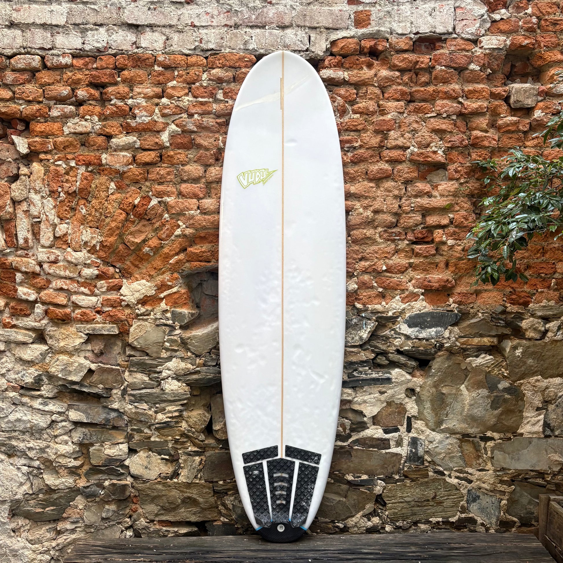 White surfboard with black and yellow design leaning against a rustic brick wall.