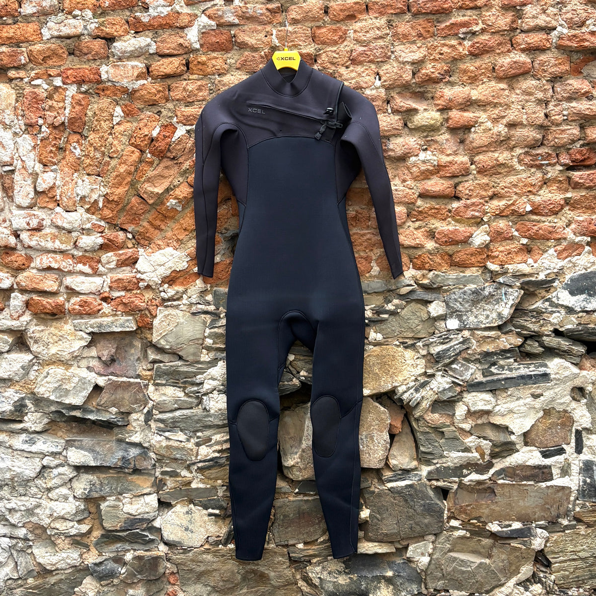 A black full-body wetsuit with long sleeves and knee patches hanging on a brick and stone wall.