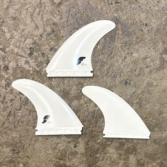 Three white surfboard fins with a logo on a textured brown surface