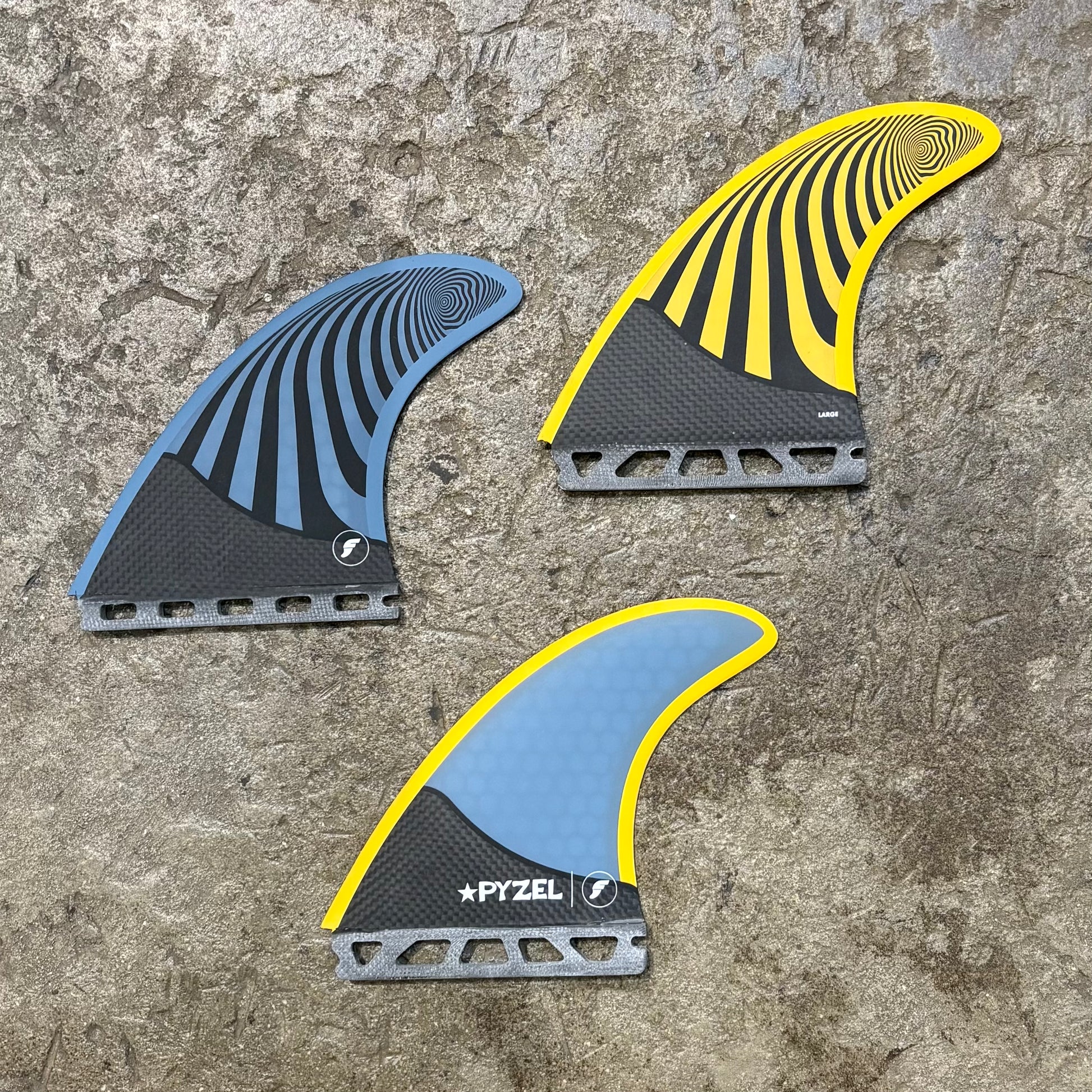 A set of three surfboard fins with a honeycomb structure and carbon fiber at the base, featuring blue and yellow coloration and the brand name 'Pyzel'.