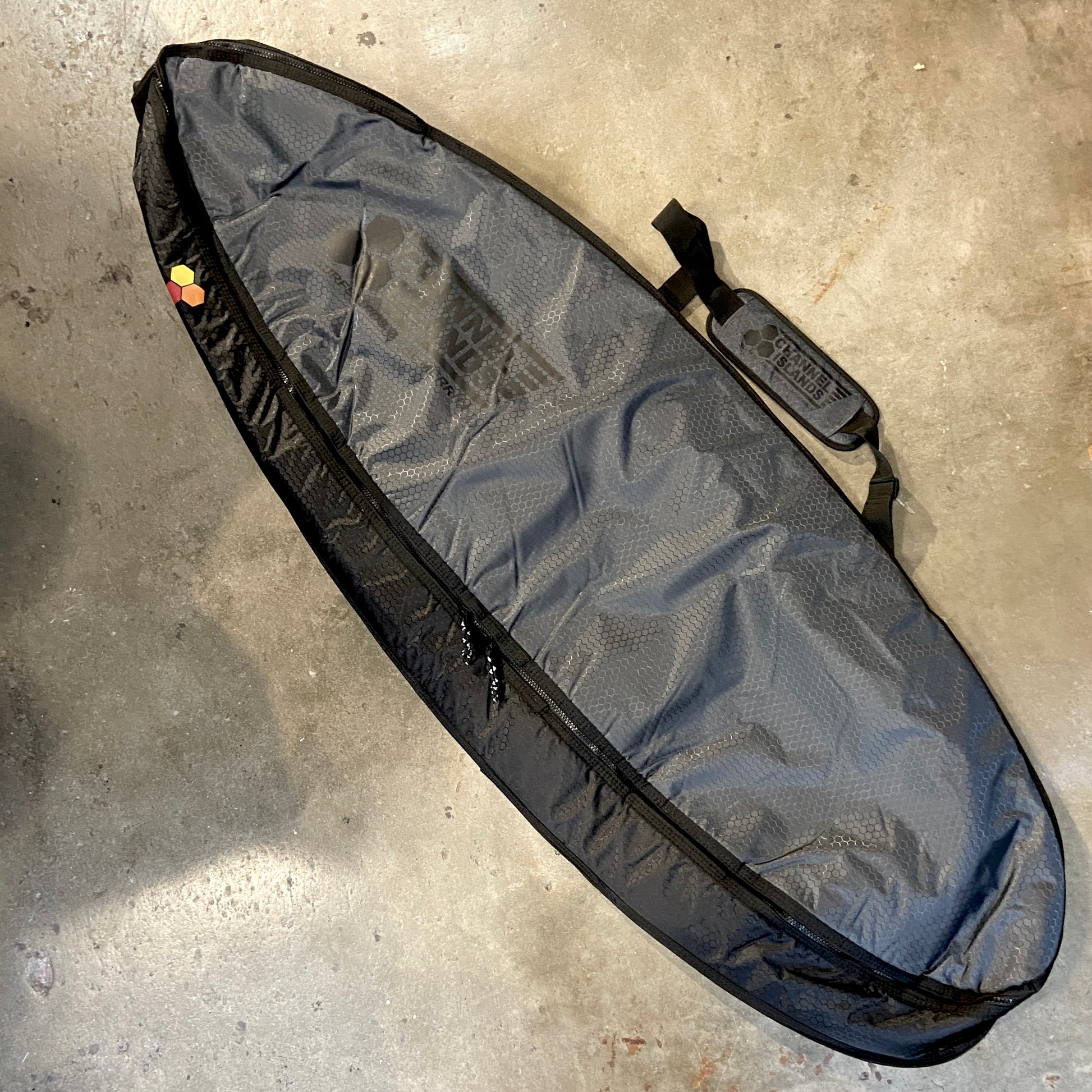 A gray surfboard travel bag with black trim and a Channel Islands logo, featuring straps and a zipper.