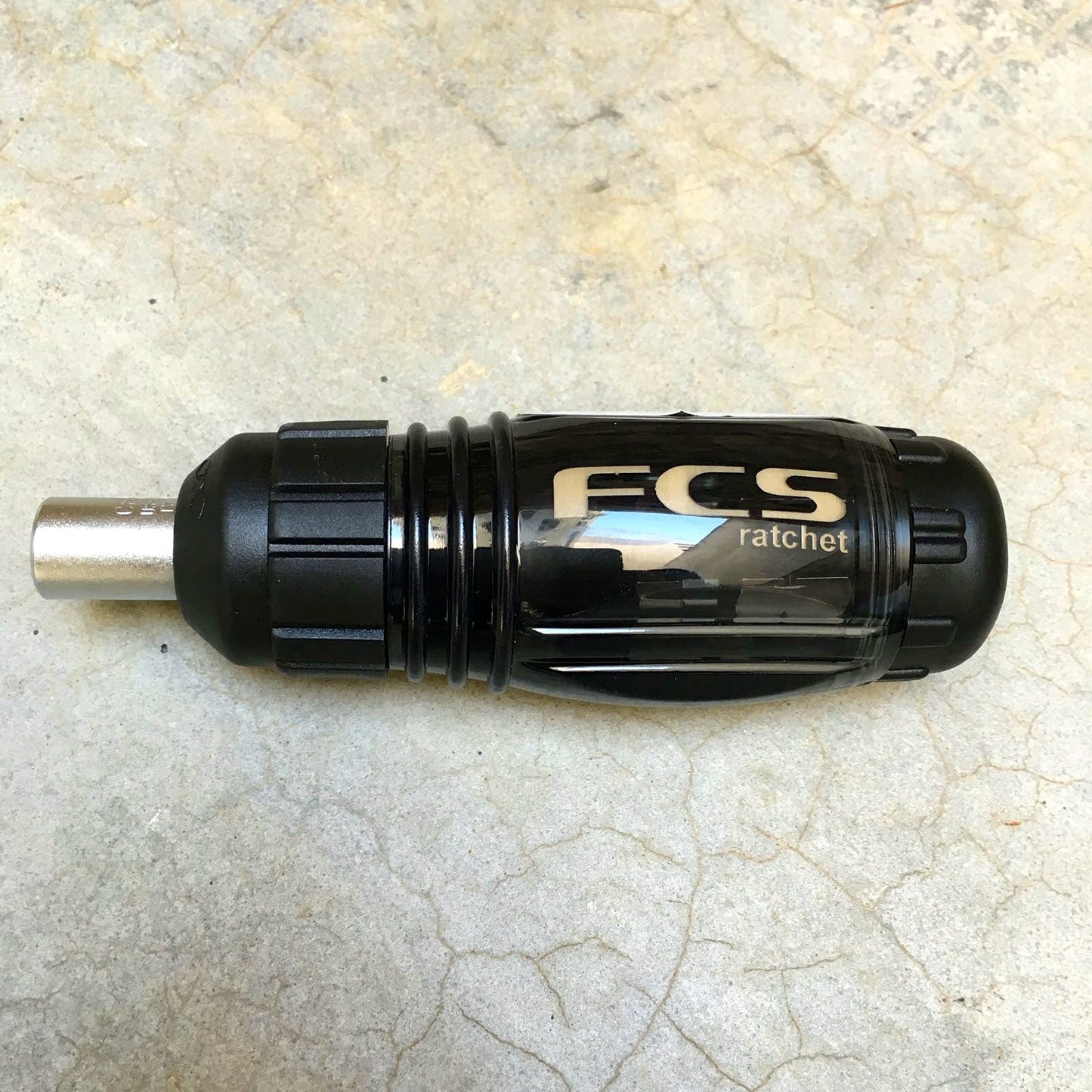 A FCS Ratchet Tool black with cream writing laid on a concrete floor