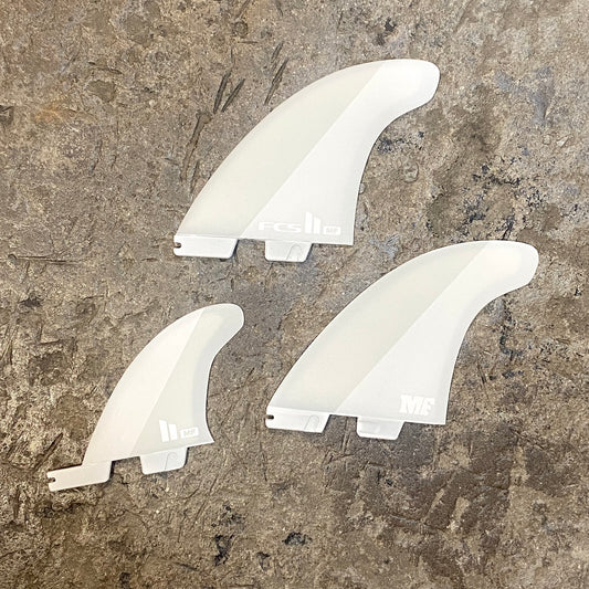 A set of FCS ll Mick Fanning Twin +1 in a white colour way laid out on a concrete floor