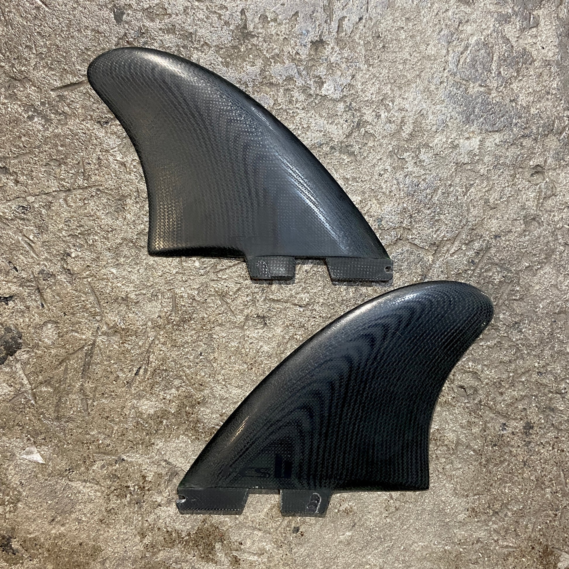 A set of FCS ll Modern Keel Fins in a black colour way laid out on a concrete surface