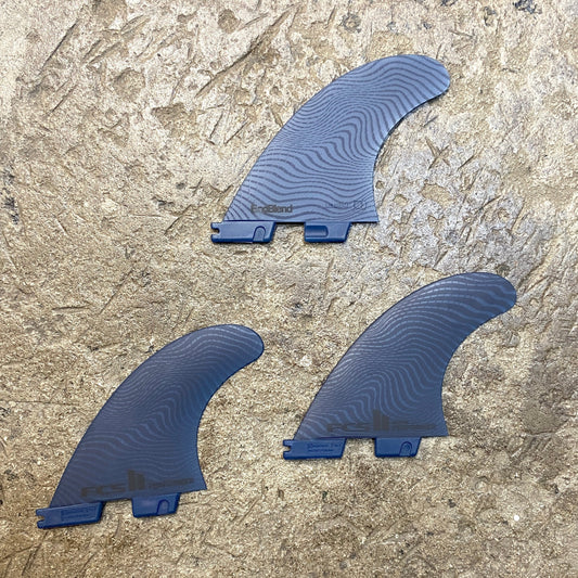 View of the FCS ll Performer Neo Glass Eco Tri Fins L in a blue colour way laid out on a concrete floor.