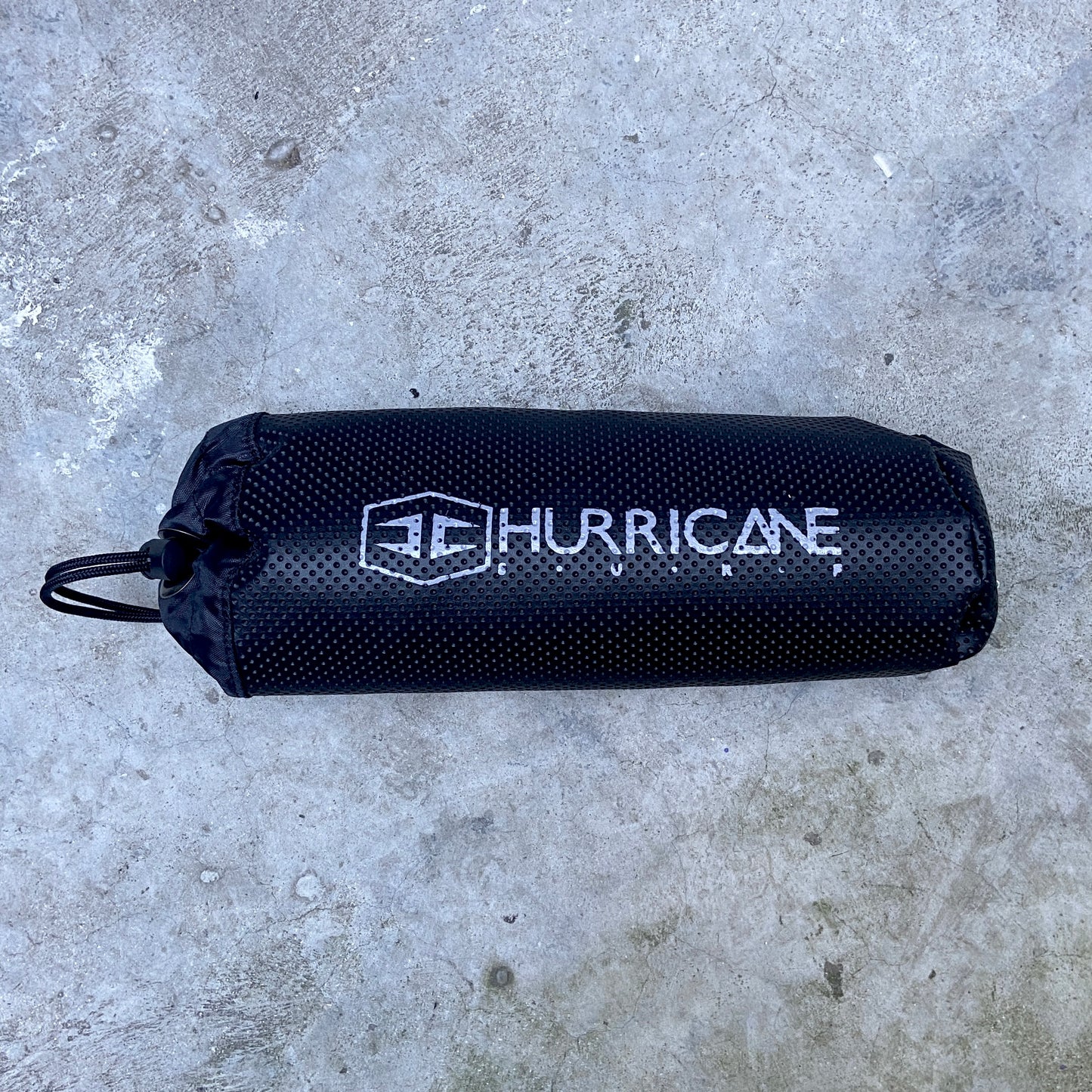 A black Hurricane wetsuit changing mat with the brand logo printed in white on the side, placed on a textured surface.
