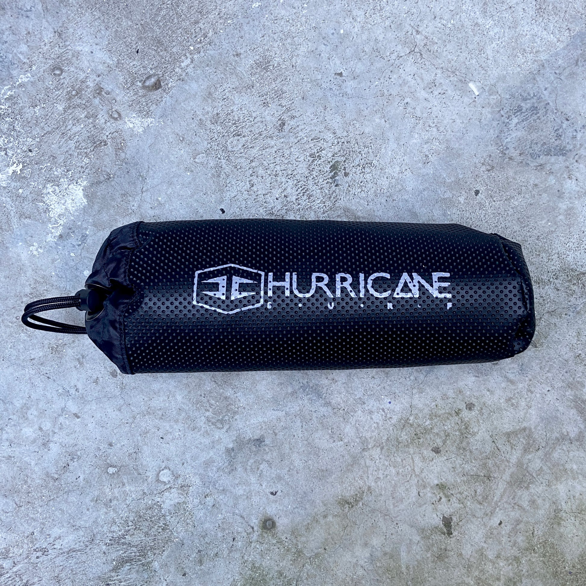 A black Hurricane wetsuit changing mat with the brand logo printed in white on the side, placed on a textured surface.