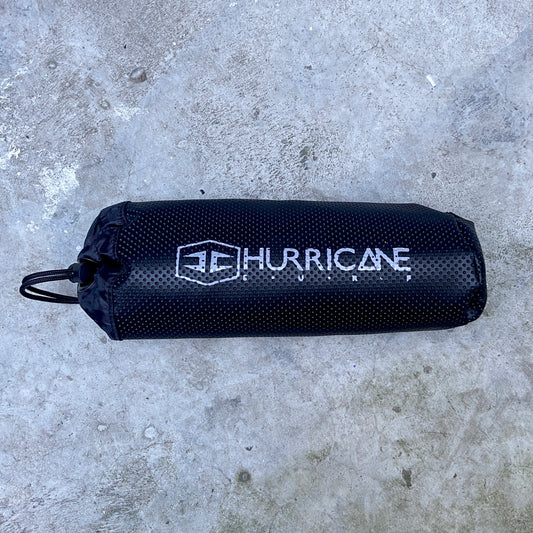 A black Hurricane wetsuit changing mat with the brand logo printed in white on the side, placed on a textured surface.