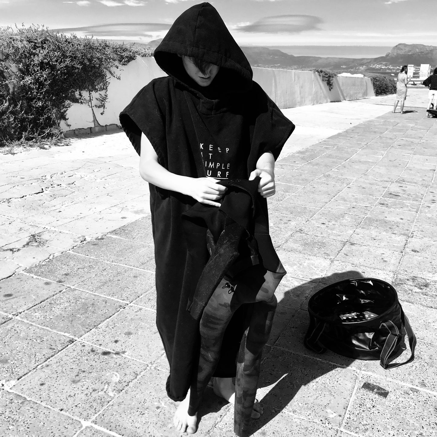 Boy wearing a KISS SURF PONCHO in BLACK standing on a pavement.