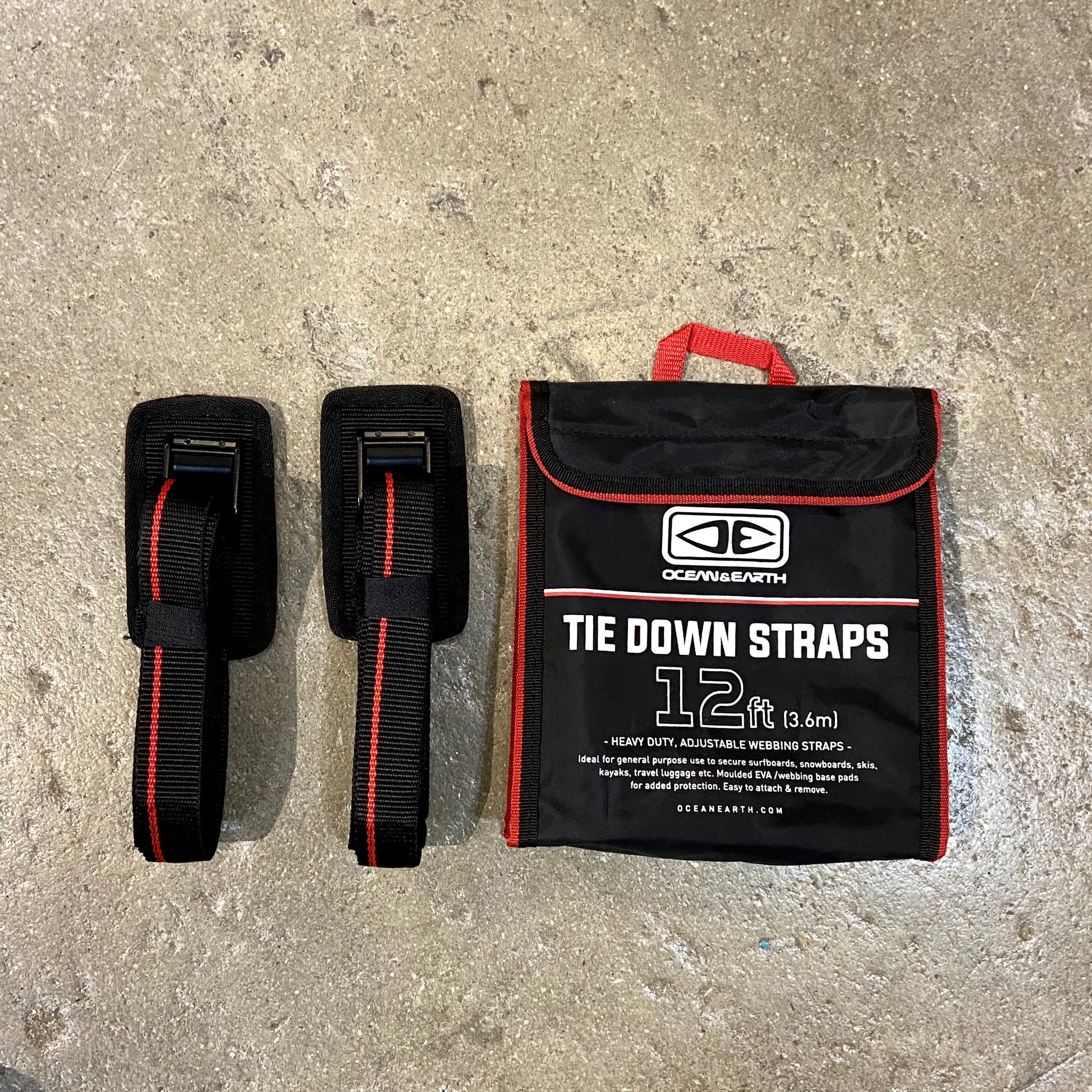 A set of black and red OCEAN&EARTH tie down straps with a protective rubber cam buckle, alongside a storage bag with the product information visible.